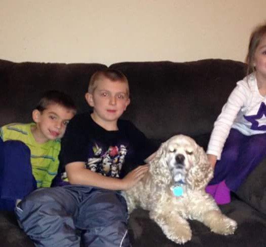 Three children sitting on a couch with a dog.