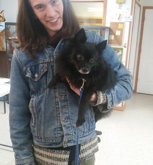 A young man holding a black dog in a denim jacket.