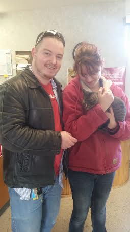 A man and woman standing next to a cat in a waiting room.