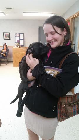 A woman holding a black puppy in an office.