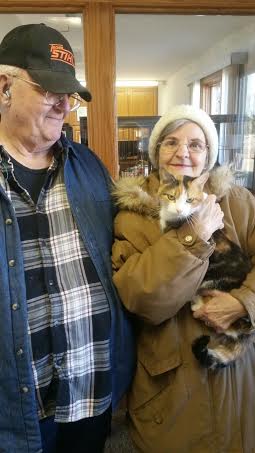 An older couple holding a cat in a library.