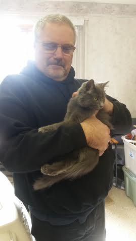 A man holding a gray cat in a room.