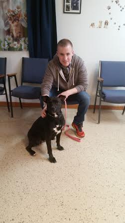 A man kneeling down next to a black dog in a waiting room.