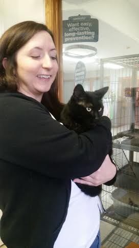A woman holding a black cat in front of a cage.