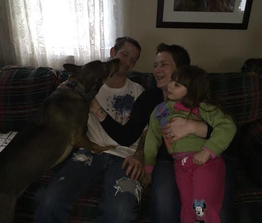 A family sits on a couch with a dog.