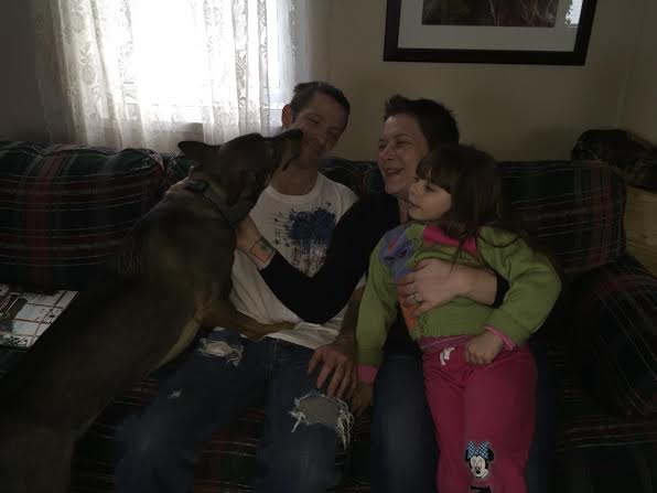 A family sits on a couch with a dog.