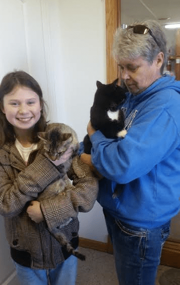 A woman holding a cat and a girl in front of a door.