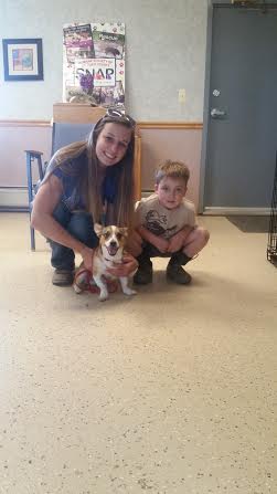 A woman and a boy pose with a dog in a vet's office.