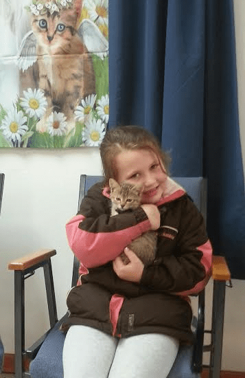 A small girl holding a cat and sitting on a chair