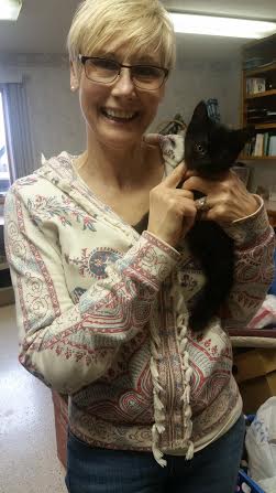 A woman holding a black kitten in a room.