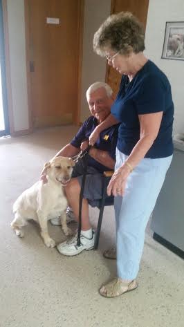 A man and woman sitting in a chair with a yellow labrador retriever.