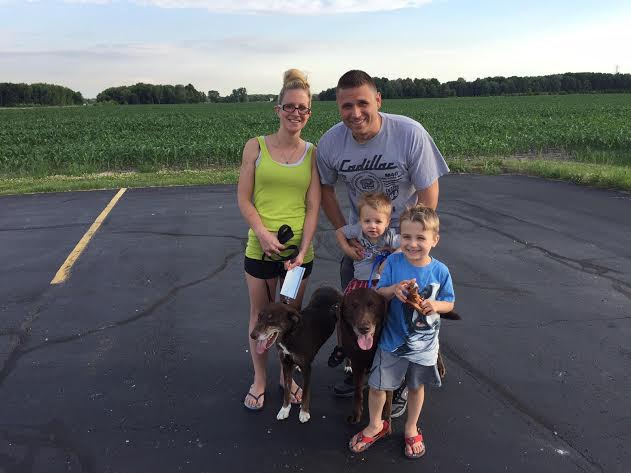 A family posing with their dogs in a parking lot.