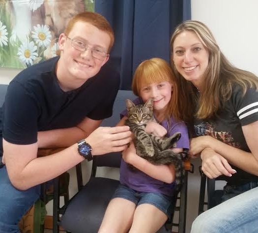 A man, woman, and child pose with a cat in a waiting room.