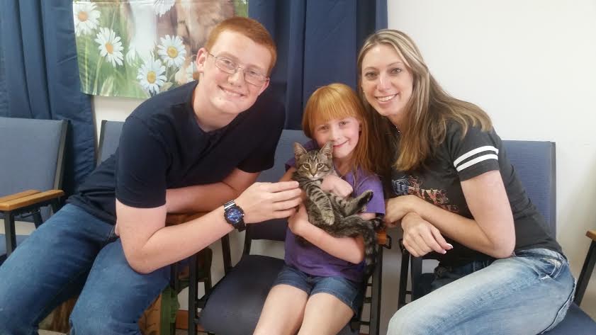 A man, woman, and child pose with a cat in a waiting room.