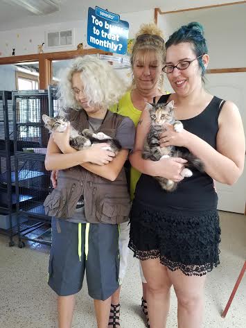 Three women holding kittens in a kennel.