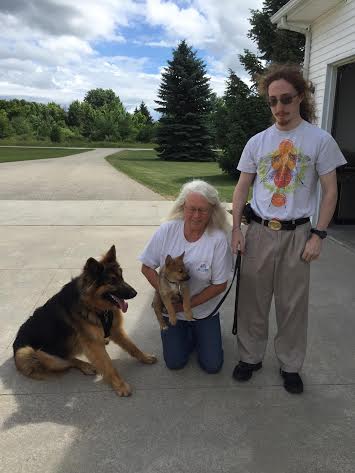 A man and woman pose with two dogs in a driveway.