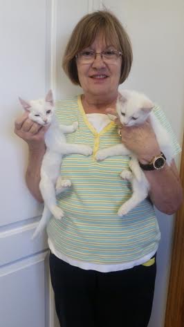 A woman holding two white kittens in front of a door.
