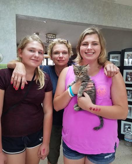 Three women are posing with a cat in a lobby.