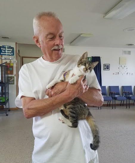 A elder man holding a cat in the room