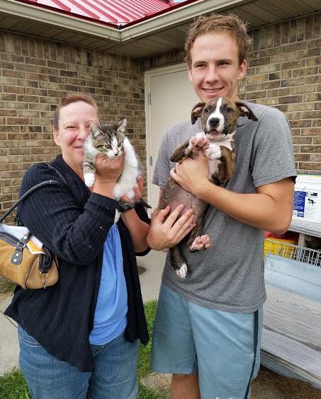 A man and woman holding two dogs and a cat.