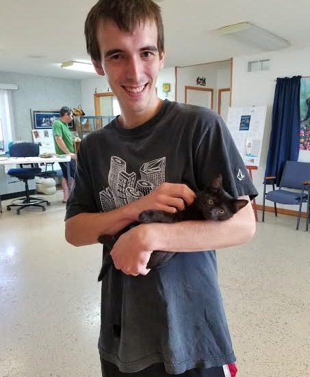 A young man holding a black cat in a room.