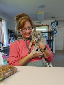 A woman sitting at a table holding a gray cat.