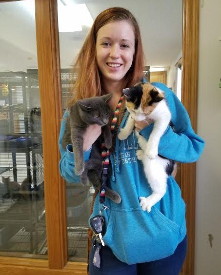 A woman holding two cats in a room.