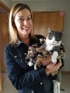 A woman holding a gray and white cat in a blanket.