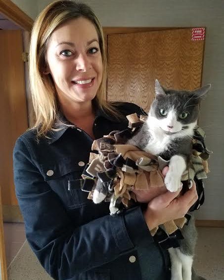 A woman holding a gray and white cat in a blanket.