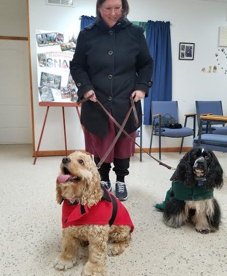 An elder woman holding two dogs in leash