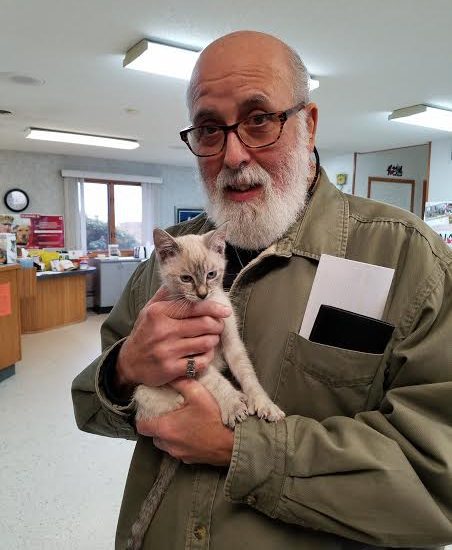 An older man holding a kitten in a room.