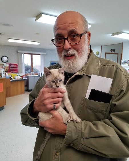 An older man holding a kitten in a room.