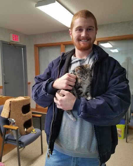 A man holding a kitten in an office.