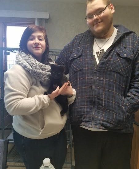 A couple holding a black cat in a room