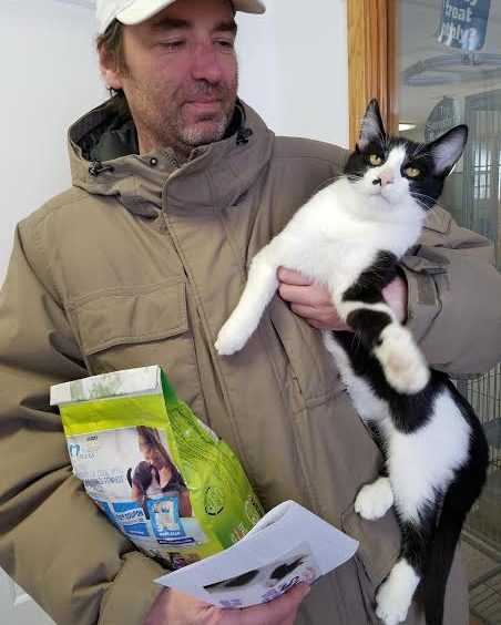 A man holding a black and white cat with a bag of food.