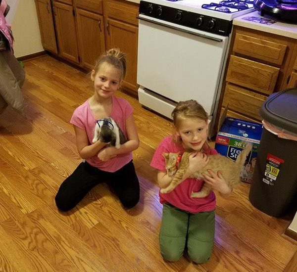 Two kids holding cats and sitting on the floor