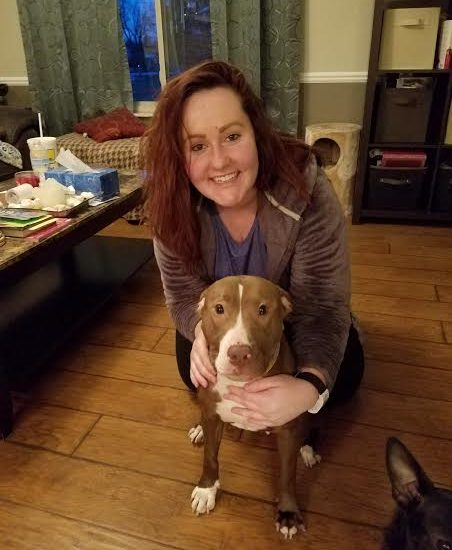 A woman kneeling down next to a pit bull terrier in a living room.