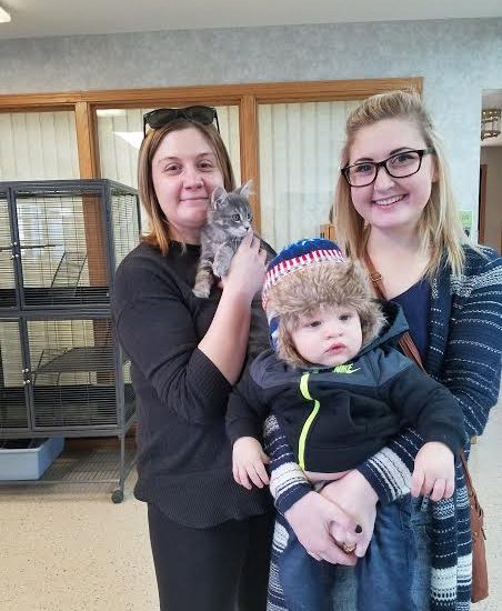Three women holding a baby and a cat in an animal shelter.