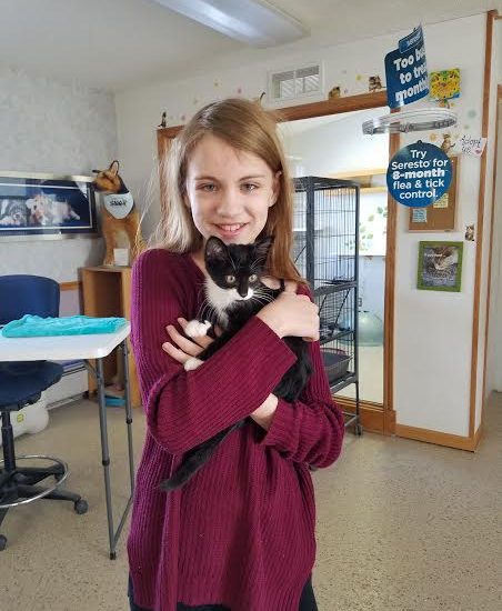 A girl holding a black and white cat in a room.