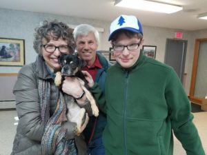 Three people standing in a room with a dog.