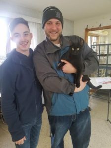 A man holding a black cat in a room.