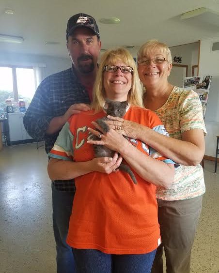 Three people standing in a room holding a kitten.