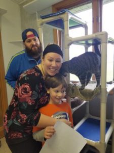 A family with a cat posing in front of a cat tower.