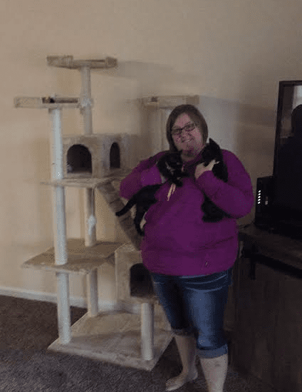 A woman standing in front of a cat tree.