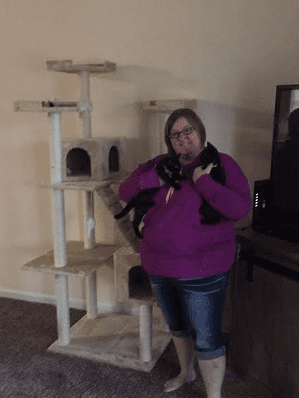A woman standing in front of a cat tree.