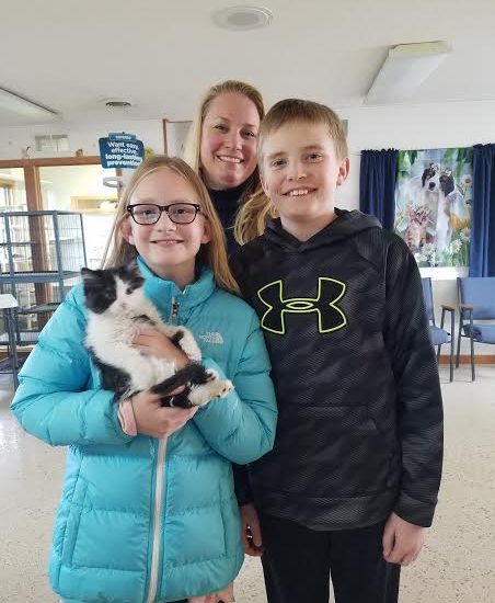 Person, person, and person pose with a black and white kitten.