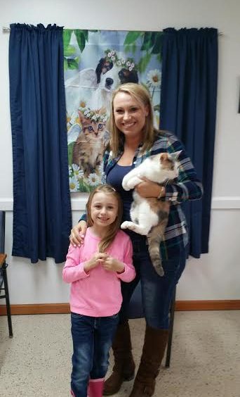 A woman and a girl standing in front of a room with a cat.