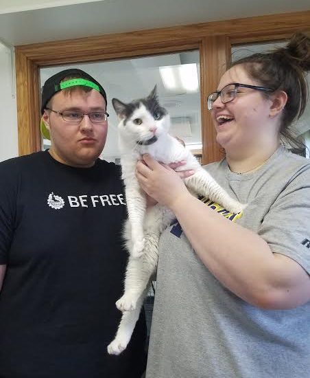 A man and woman are holding a cat in an office.