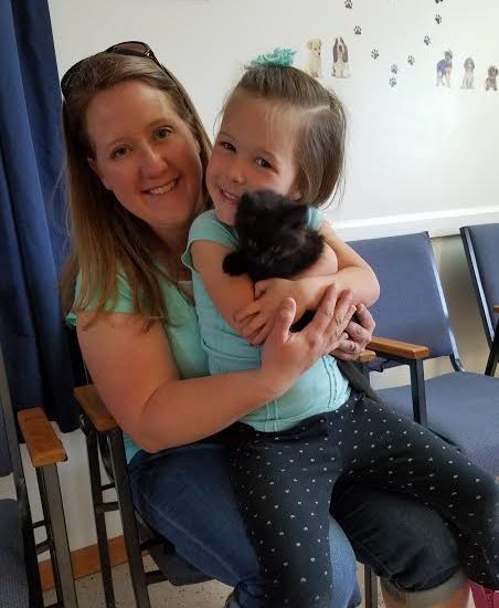 A woman holding a black kitten in a waiting room.