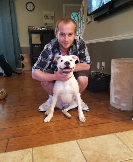 A man kneeling down next to a white dog in a living room.